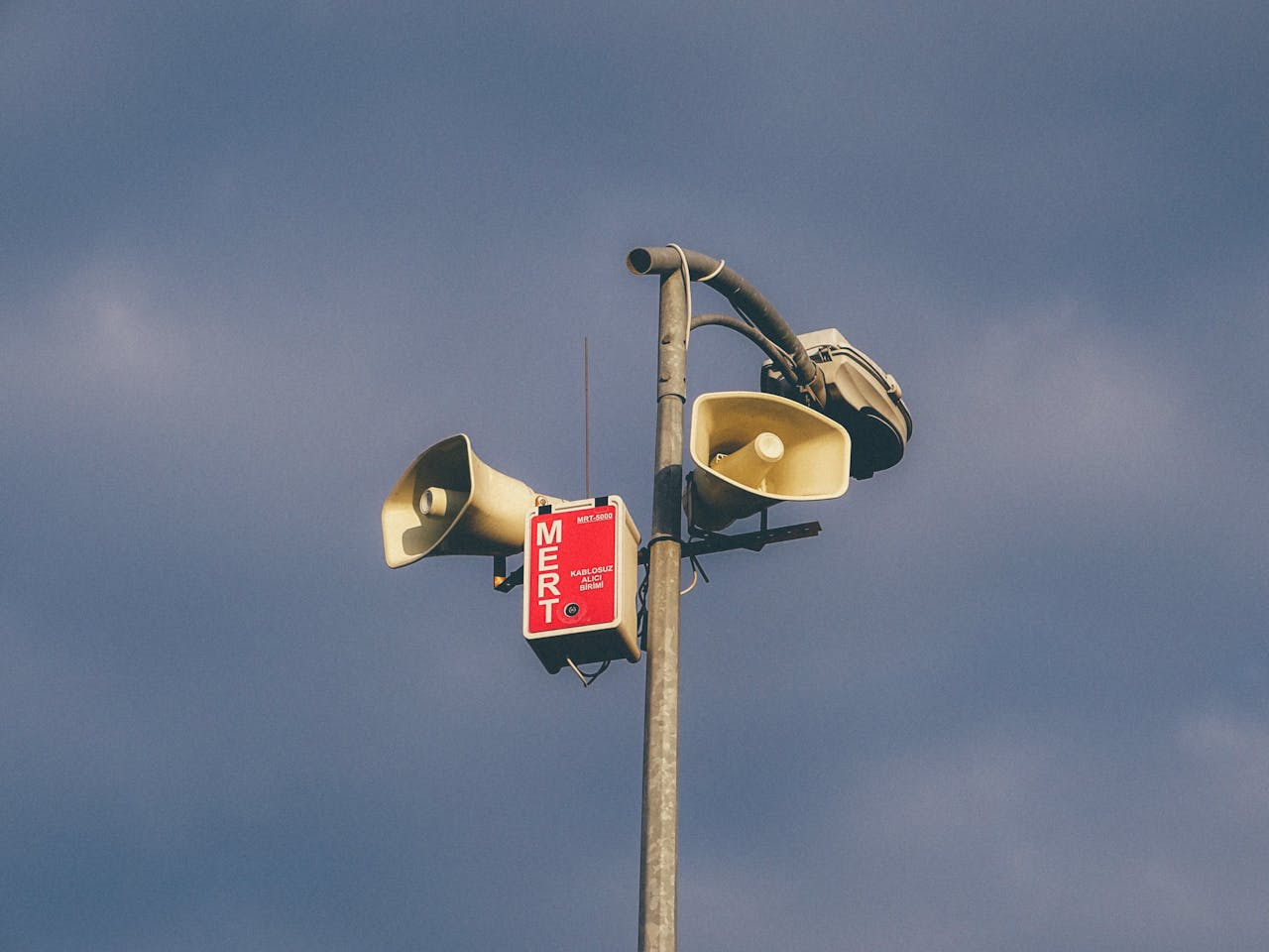 Mastering the First Impression: Your intriguing post title goes here A warning system with loudspeakers on a pole against a cloudy sky, signaling emergency alerts.